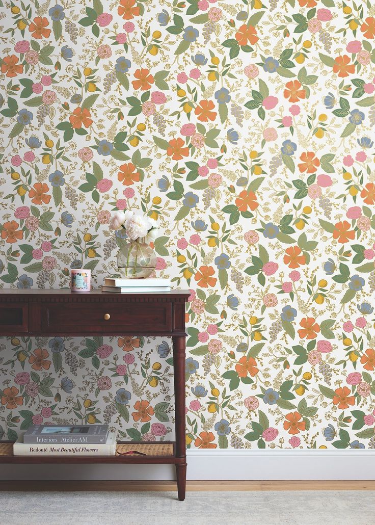 a table with a book on it in front of a floral wallpaper