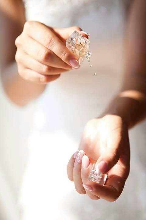 a woman in a wedding dress holding an ice cube with her fingers and fingernails