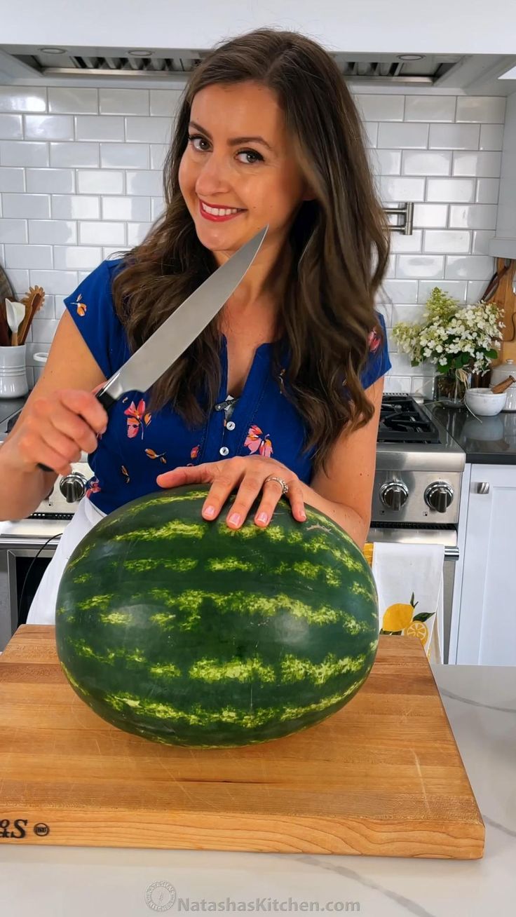 a woman cutting up a large watermelon on top of a wooden cutting board