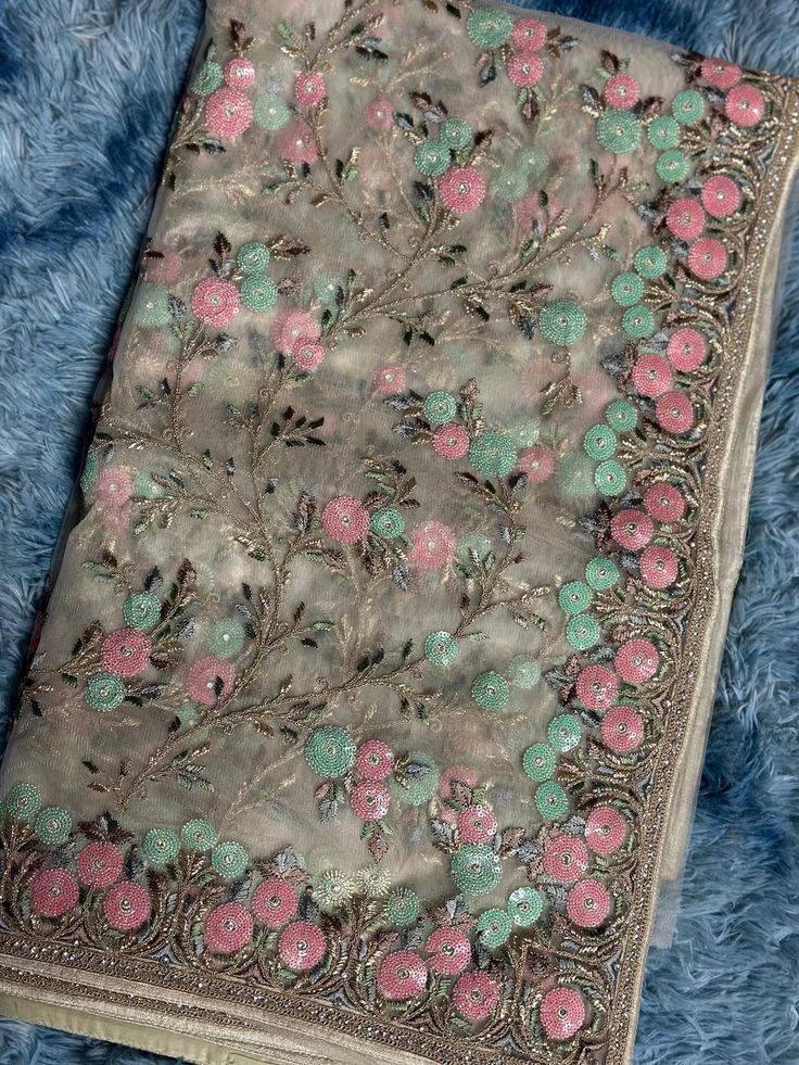 an embroidered cloth with pink flowers and green leaves on blue furnishing next to a pair of scissors