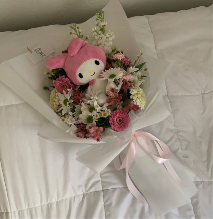 a bouquet of flowers and a hello kitty stuffed animal on a bed with white sheets