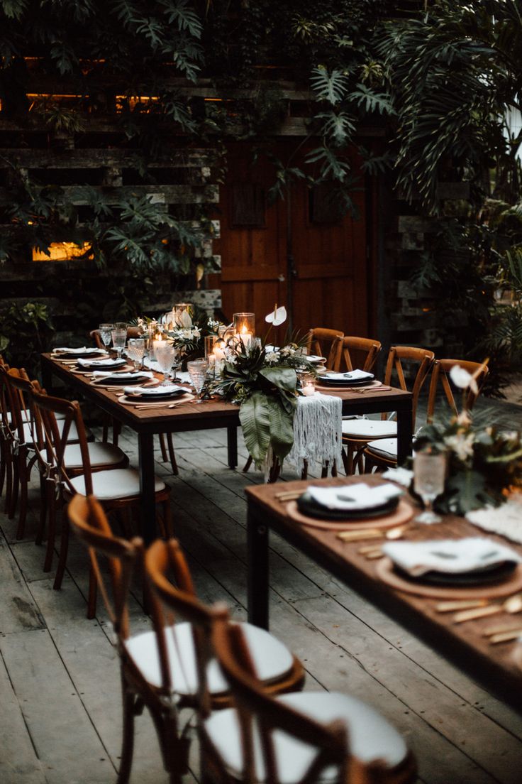 an outdoor dining area with wooden tables and white linens, candles and greenery