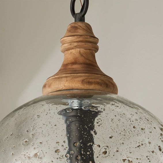 a light hanging from a ceiling fixture with water droplets on the glass and wood accents