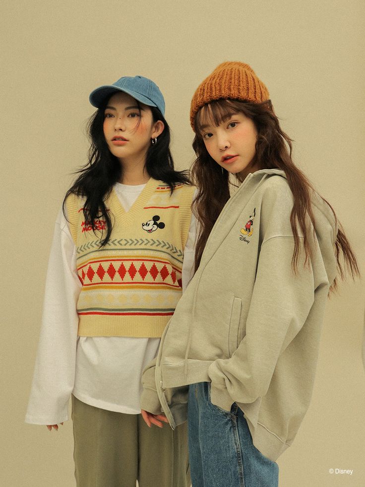 two young women standing next to each other in front of a wall wearing sweaters and hats