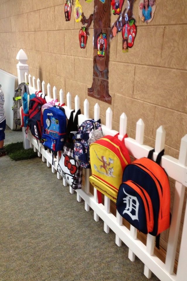 several backpacks are lined up against a white picket fence in front of a wall