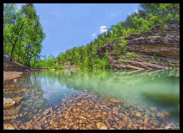 the water is crystal green and there are rocks on the bank in front of it