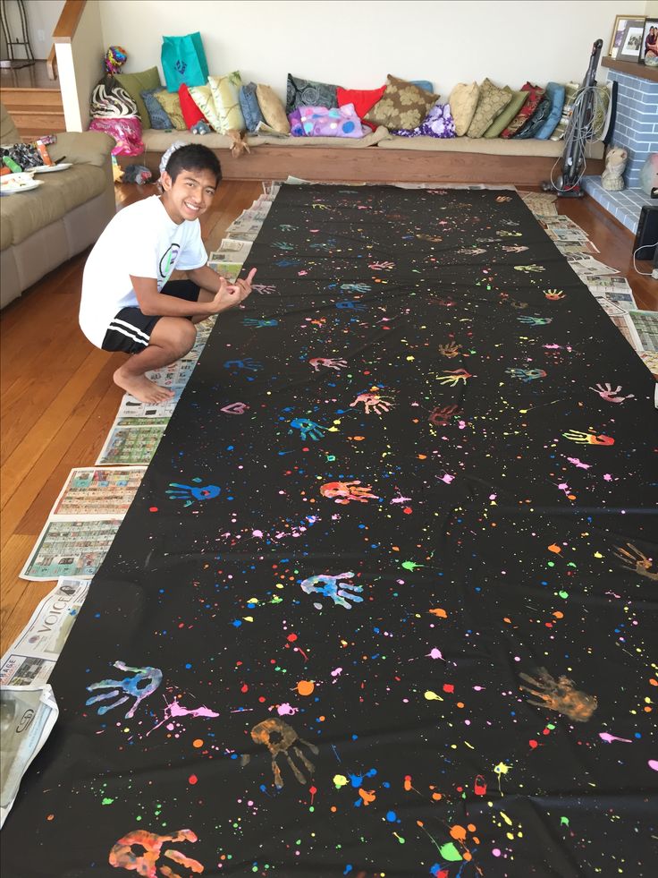 a young boy sitting on the floor next to a large rug covered in handprints