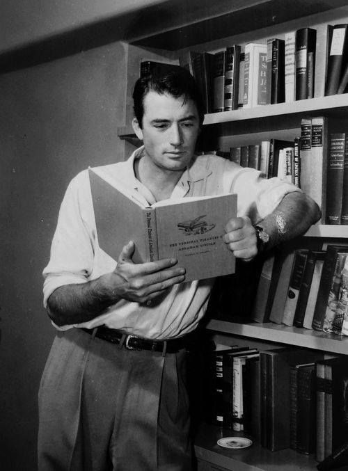 a man standing in front of a bookshelf holding a book and looking at it