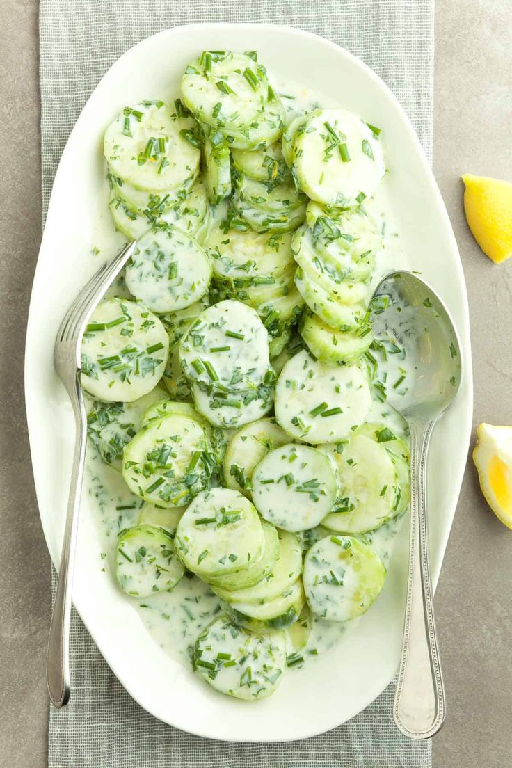 a white plate topped with cucumbers covered in sauce next to lemon wedges