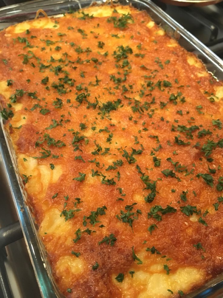 a casserole dish with cheese and parsley on top is sitting on the stove