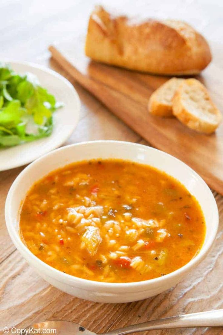 there is a bowl of soup on the table with bread and salad in the background