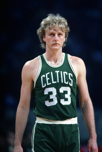 a man in a green jersey standing on a basketball court with his hands behind his back