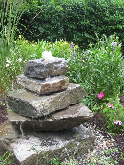 some rocks are stacked on top of each other in a garden with flowers and plants