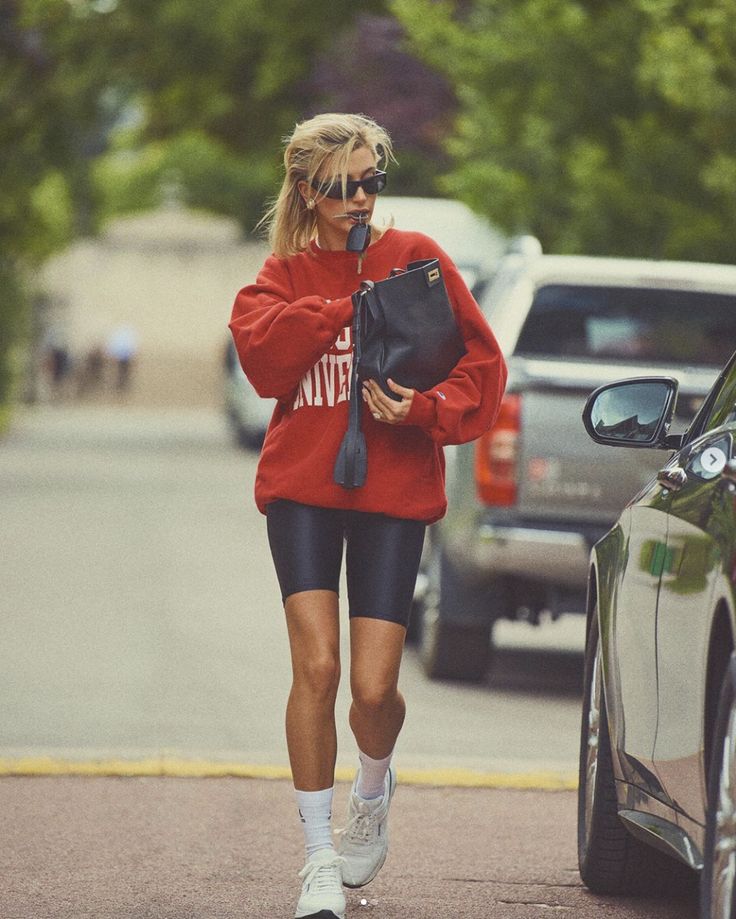 a woman walking down the street in shorts and a red sweatshirt with writing on it