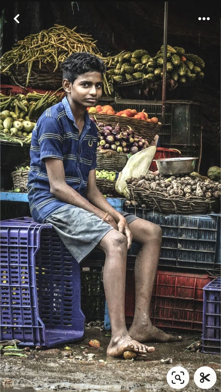 a young man sitting on top of a pile of fruit in front of a market