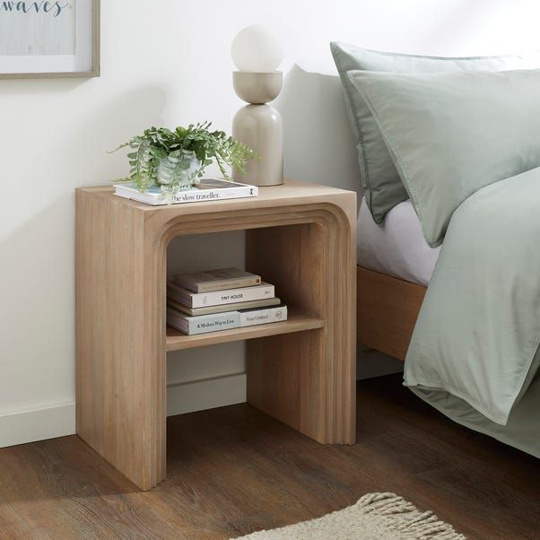 a nightstand with books on it next to a bed