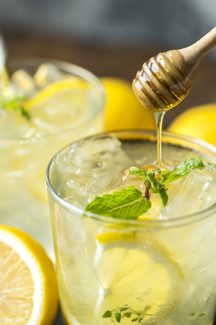 honey being drizzled over lemons in glasses filled with ice and water