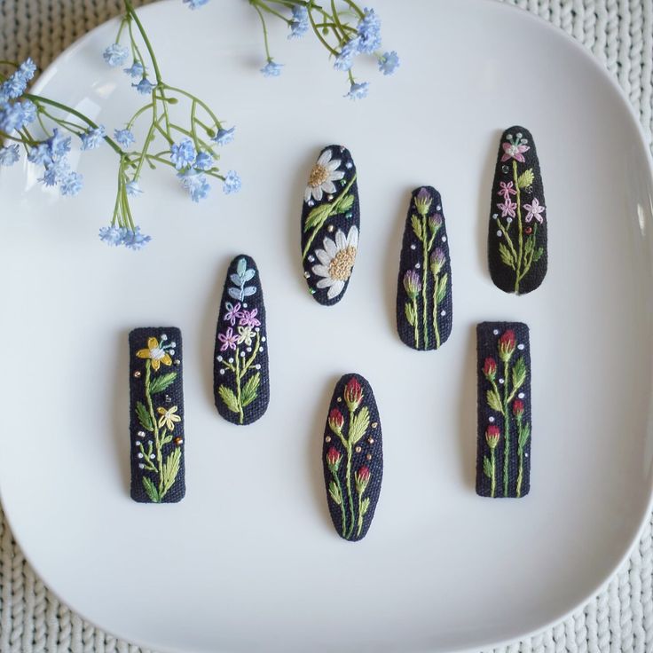 five painted nails sitting on top of a white plate next to blue and yellow flowers