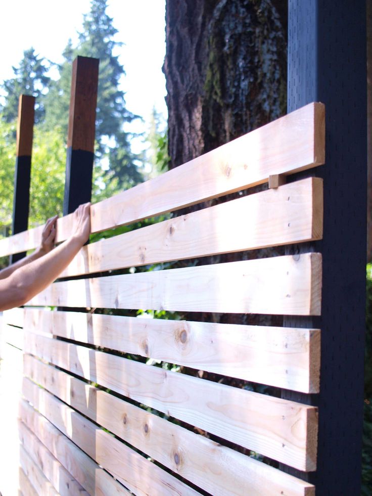 a person is placing wood on the side of a wooden fence with trees in the background