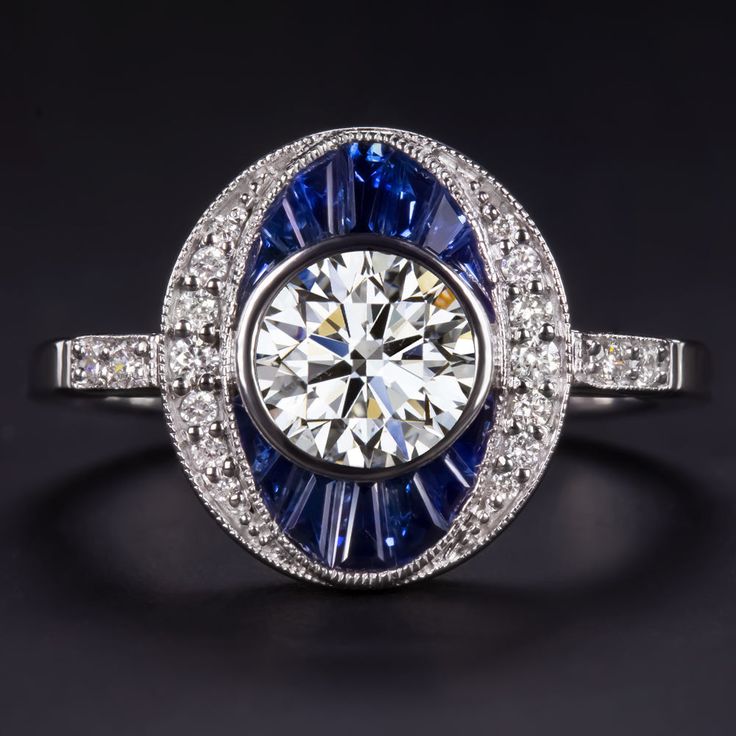 Why we love it:This diamond and sapphire ring offers a stunning Art Deco style design, rich color, and gorgeous, substantial sparkle! Featuring a high quality round cut diamond, the ring has a beautifully crafted oval design set with brilliantly white and vibrant natural diamonds as well as rich blue custom cut natural sapphires.Highlights:- 0.90ct round cut diamond center- GIA certified- Excellent cut for fantastic sparkle- Bright white and completely eye clean with grades of G SI1- Calibre cut Vintage Diamond White Gemstone Ring, Classic Round Multi-stone Jewelry, Art Deco Gia Certified Sapphire Ring As Gift, Gia Certified Art Deco Sapphire Ring Gift, Art Deco Sapphire Jewelry Gia Certified, Classic Sapphire Cluster Ring Gia Certified, Art Deco Sapphire Ring With Gia Certified Diamond, Art Deco Gia Certified Sapphire Ring With Diamond, Classic Gia Certified Sapphire Cluster Ring