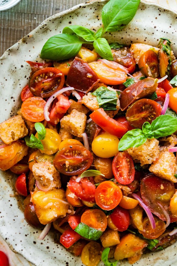 a white bowl filled with lots of food on top of a wooden table next to tomatoes and other vegetables