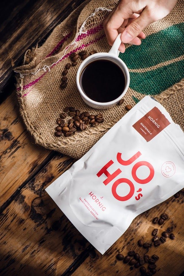 someone is holding a spoon over a bag of coffee on a wooden table next to a cup of coffee