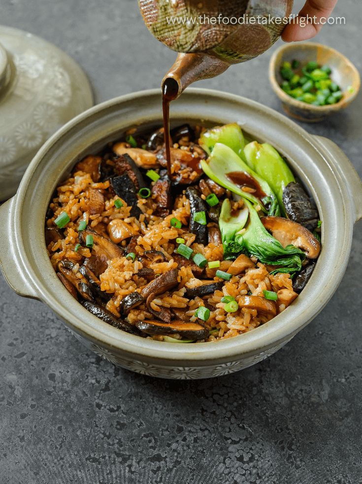 someone pouring sauce into a bowl filled with rice and vegetables