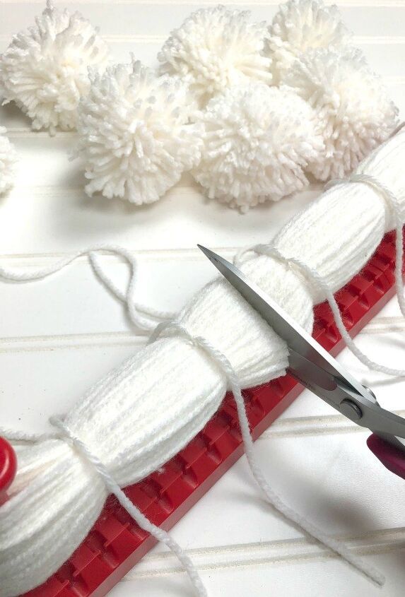 a pair of scissors sitting on top of a red and white piece of fabric next to some pom - poms