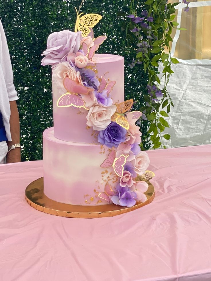 a three tiered cake with flowers and butterflies on it sitting on top of a table