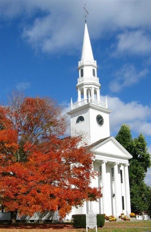 a white church with a steeple and clock on it's side in the fall