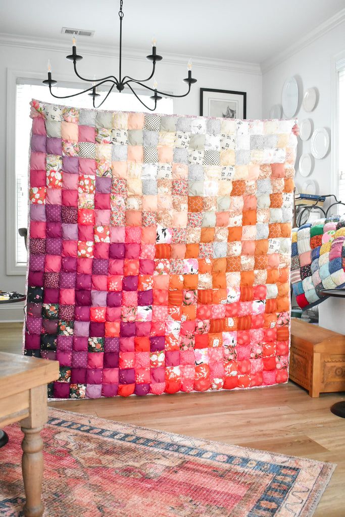 a large multicolored quilt hanging on the wall next to a wooden table and rug