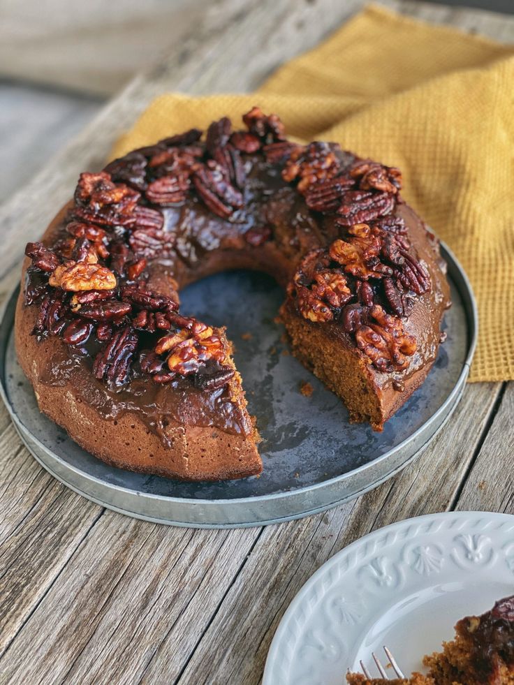 a bundt cake with pecans on top is sitting on a plate next to a fork