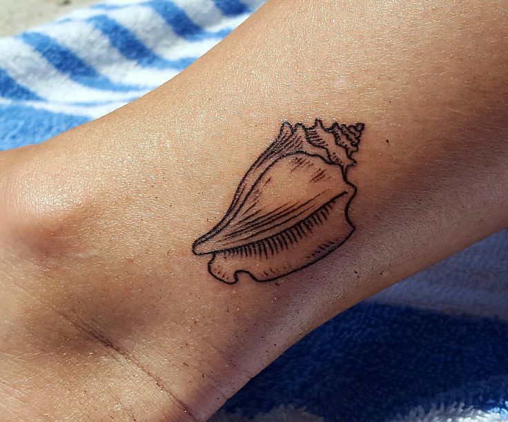 a small tattoo on the foot of a woman's left leg with a sea shell