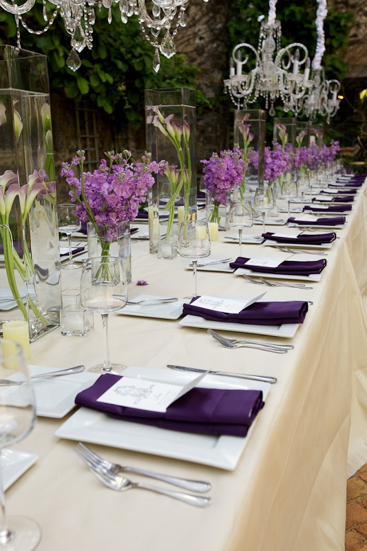 the table is set with purple flowers and place settings