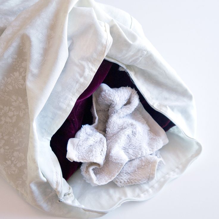 a white teddy bear laying inside of a bag on top of a table next to a purple blanket