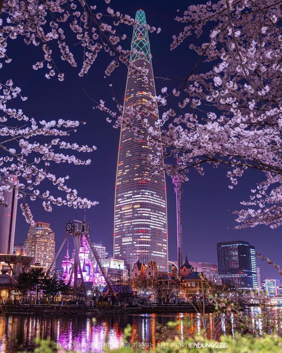 the skyscraper is lit up at night with cherry blossom trees in full bloom around it