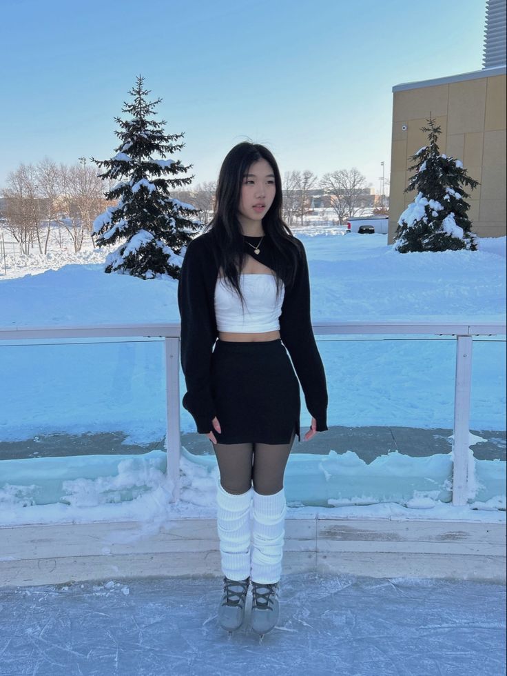 a woman standing in the snow wearing knee high boots and a white top with short sleeves