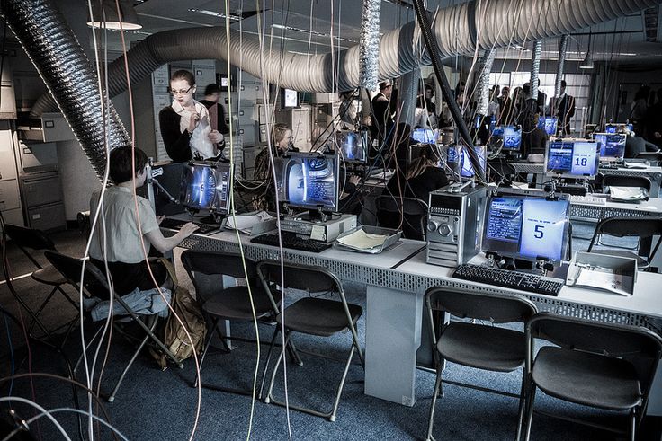 people sitting at desks with computers and wires hanging from the ceiling in an office