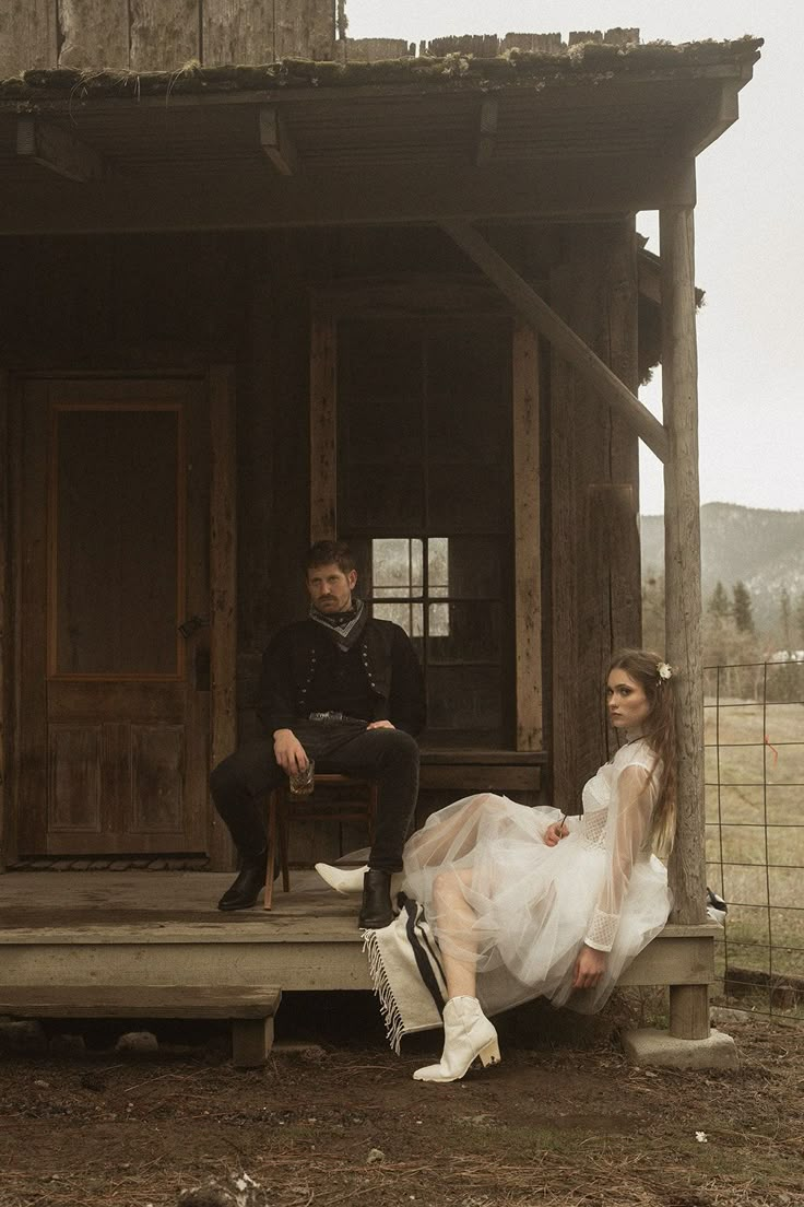 a man and woman sitting on a porch next to each other in front of a cabin