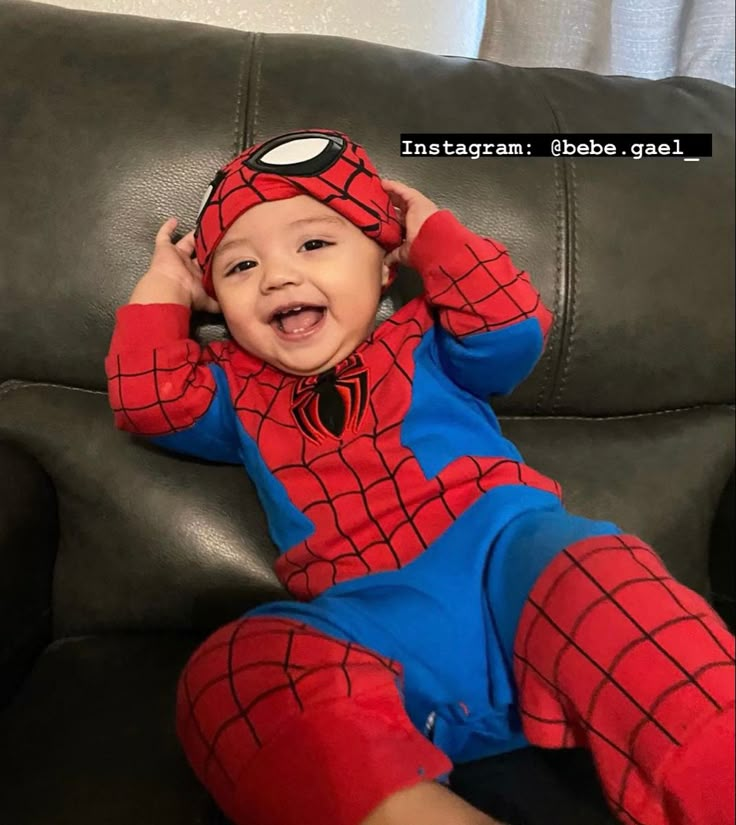 a baby in a spiderman costume sitting on a couch with his hands behind his head