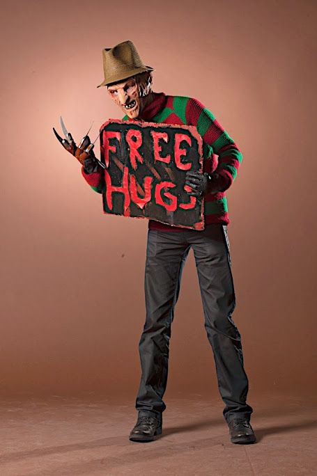 a man dressed as a zombie holding a free hugs sign with his hands and wearing a fedora