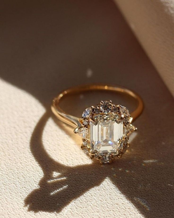 an engagement ring with a large diamond surrounded by smaller diamonds on the side, sitting on a white surface