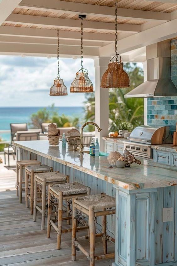 an outdoor kitchen with blue cabinets and white counter tops is featured in this photo, while the ocean sits beyond it