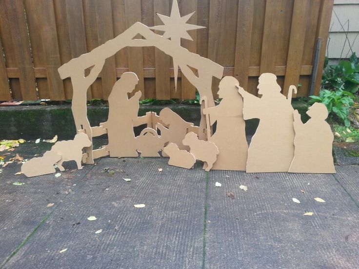 a nativity scene made out of cutouts on the ground in front of a fence