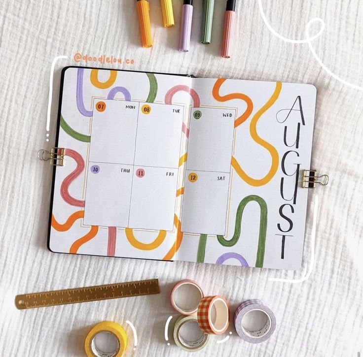 an open planner with markers, tape and washi tapes on the table next to it