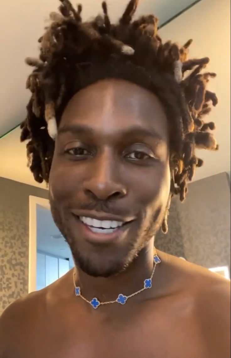 a man with dreadlocks is smiling and wearing a blue beaded choker