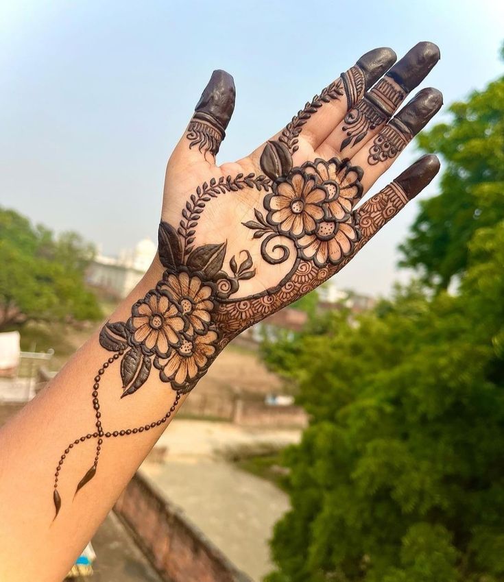 a woman's hand with henna tattoos on it and trees in the background