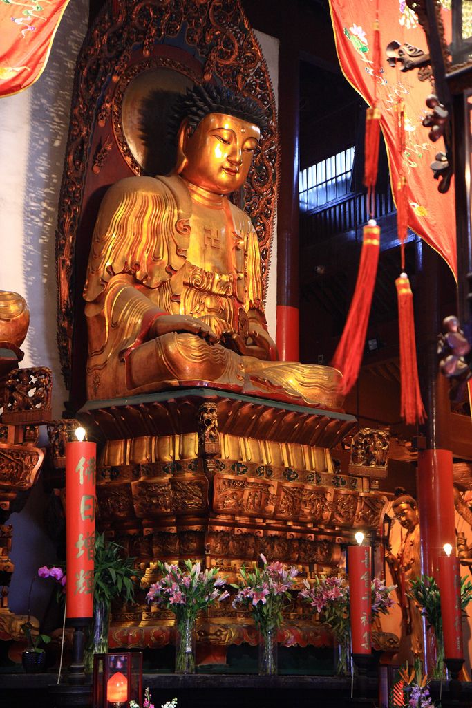 a large golden buddha statue sitting in front of some red and white curtains with candles