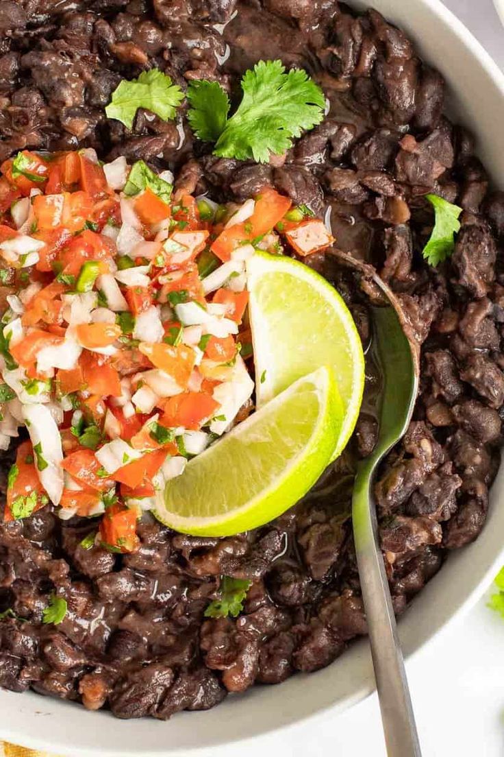 a white bowl filled with black beans, cilantro, and lime wedges