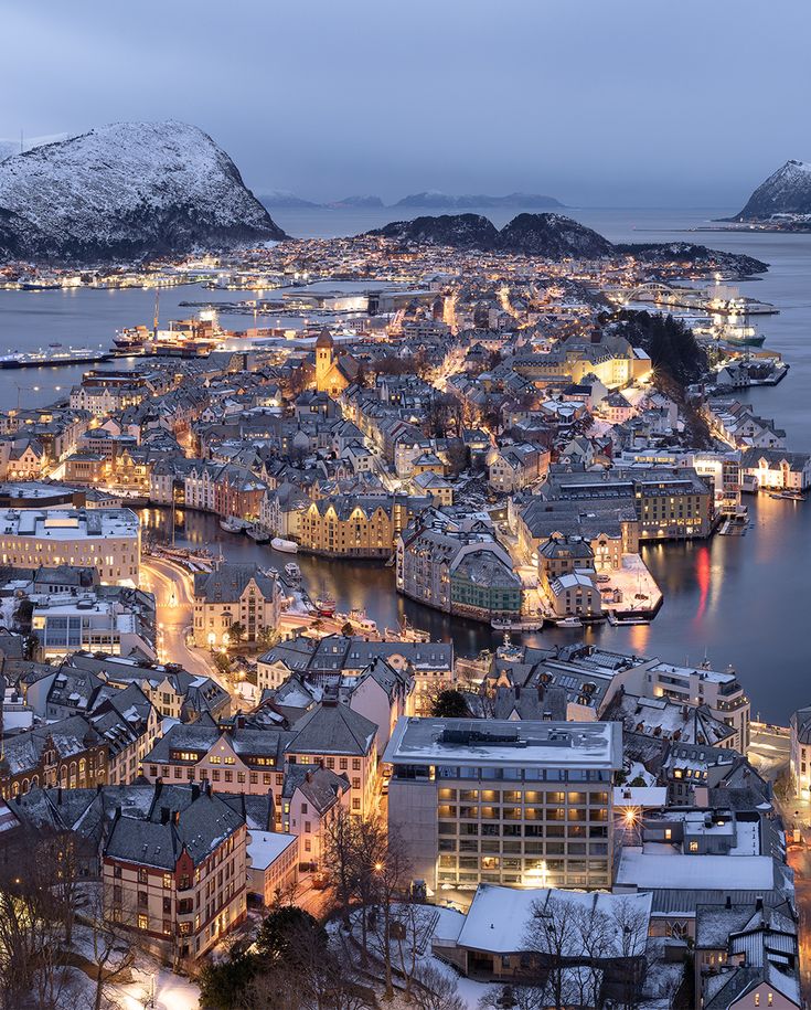 an aerial view of a city at night with snow on the ground and mountains in the background